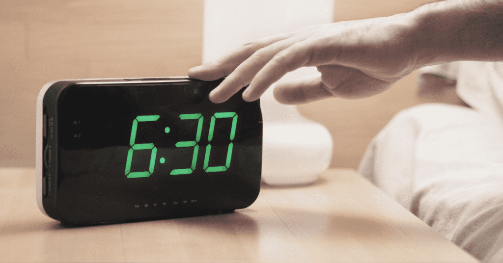 Person with their hand on an alarm clock, the time is 6:30.