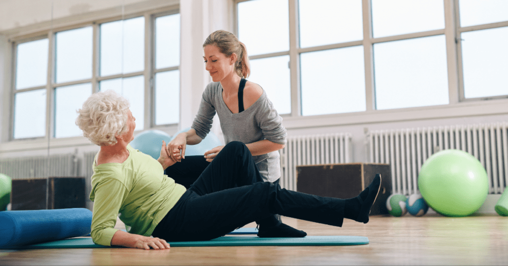 A personal trainer helping an elderly lady exercise.