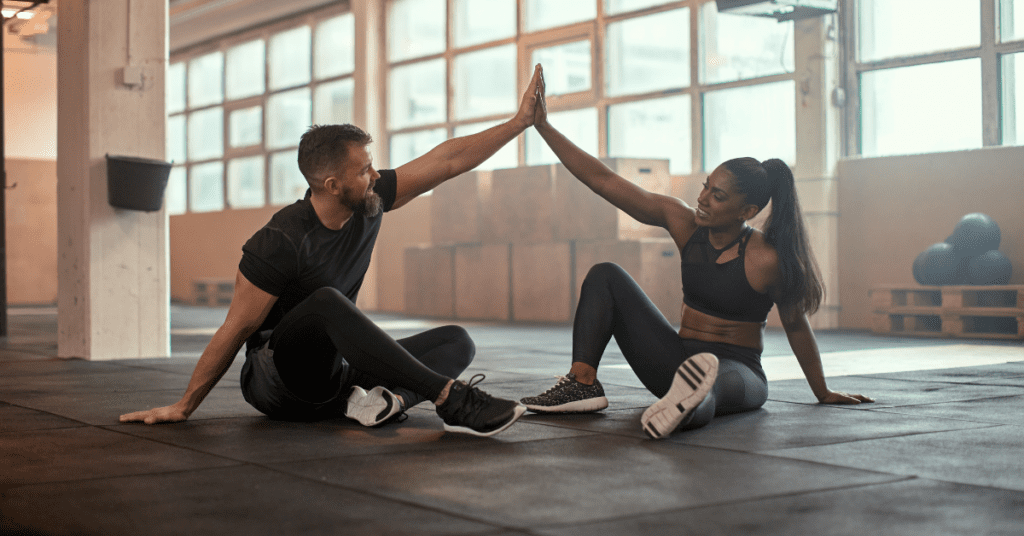Two people exercising and stretching on the floor of a gym.