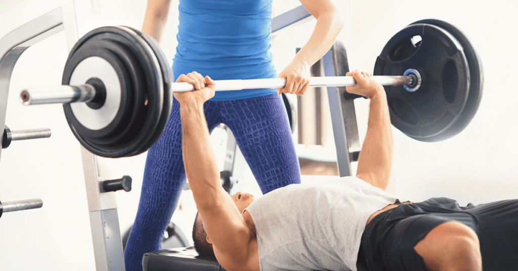 Man using the bench press machine whilst being spotted by a woman.