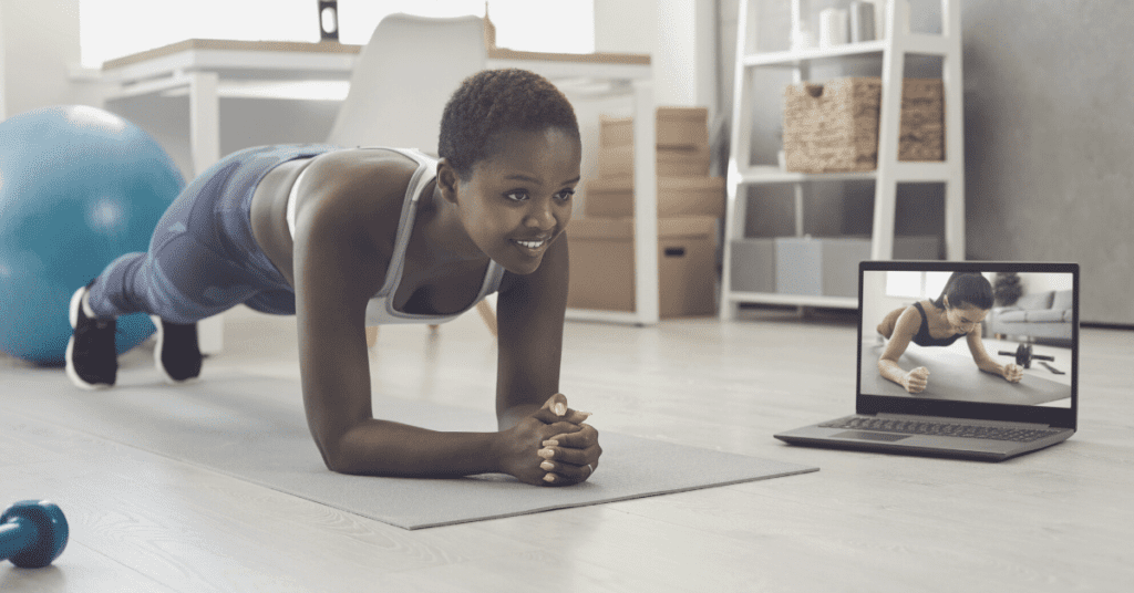 A woman exercising on the floor with an online personal trainer on the computer next to her.